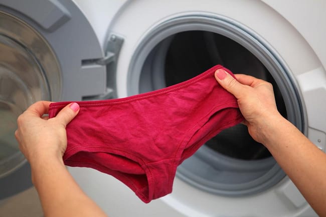 woman-holding-a-pair-of-cotton-underwear-pants-next-to-washing-machine